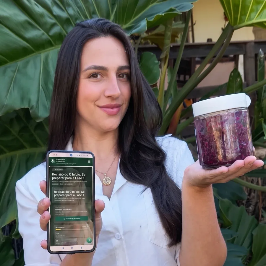Poliana ao ar livre segurando o celular com a área de membros aberta em uma das mãos e um pote de repolho roxo fermentado na outra